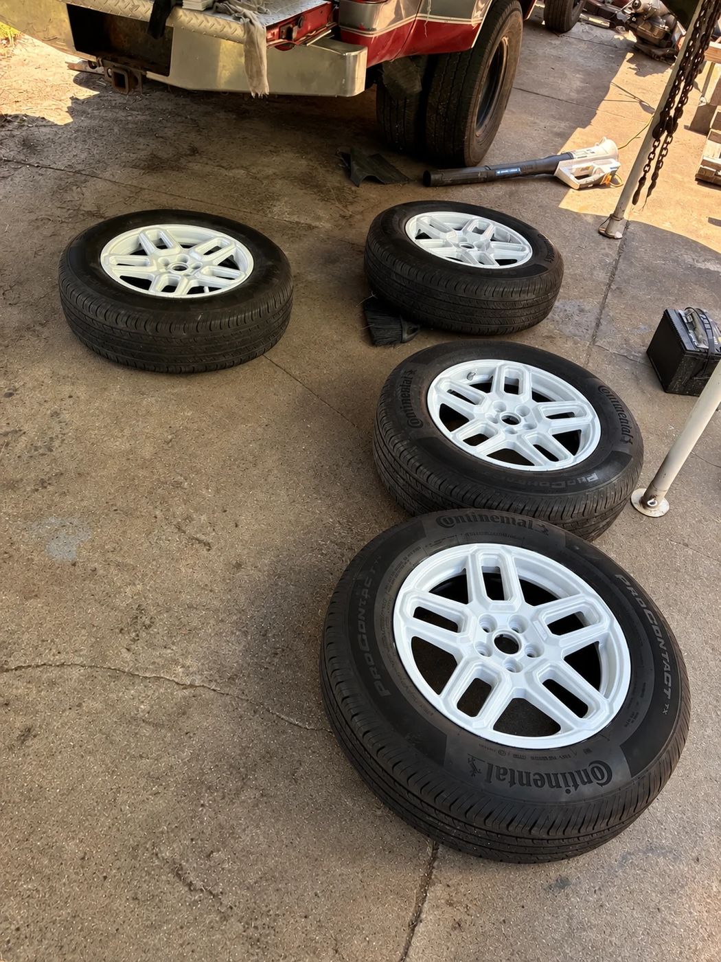 Four white wheels with new tires, off the car for service